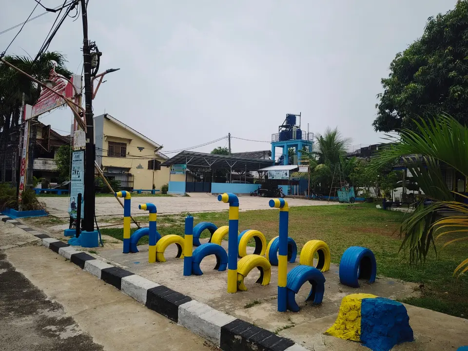 Area bermain dari ban bekas bercat biru dan kuning yang ditanam berjajar di atas rumput.