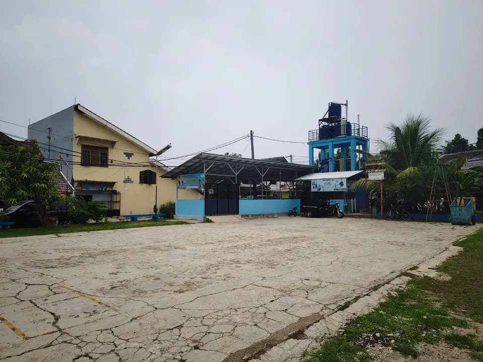 Lapangan beton serbaguna dengan menara air biru dan atap pos di belakangnya.