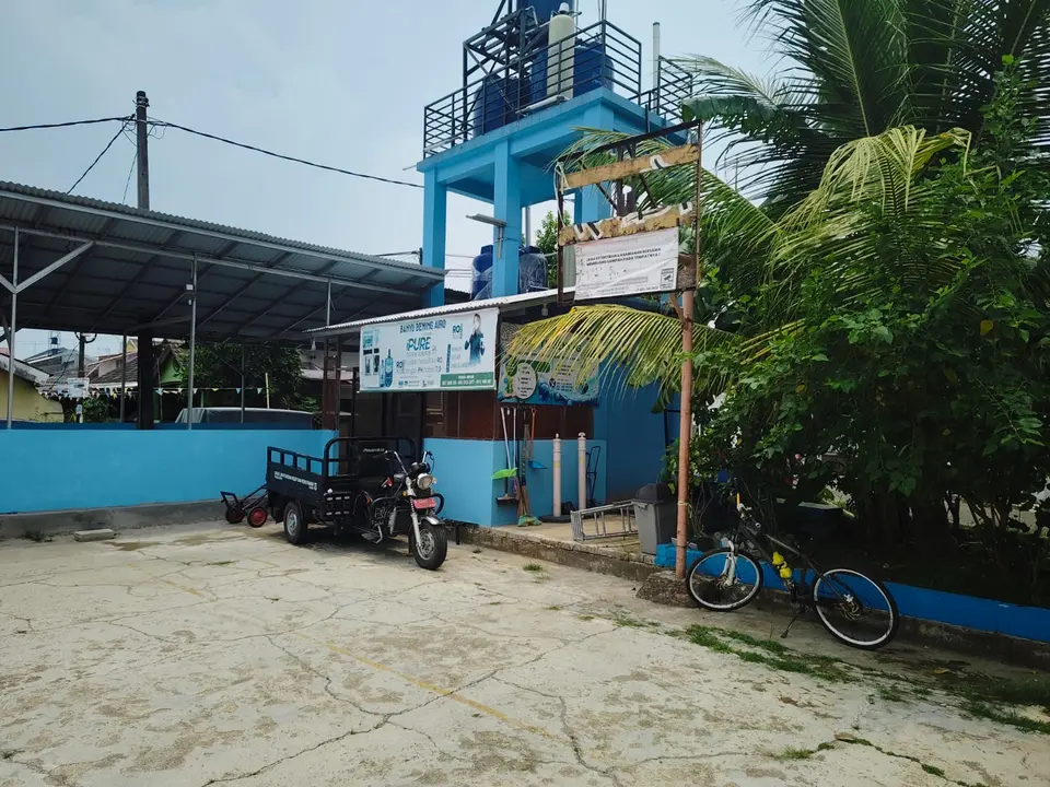 Menara air biru di sisi lapangan, dengan sepeda dan motor terparkir di depannya.