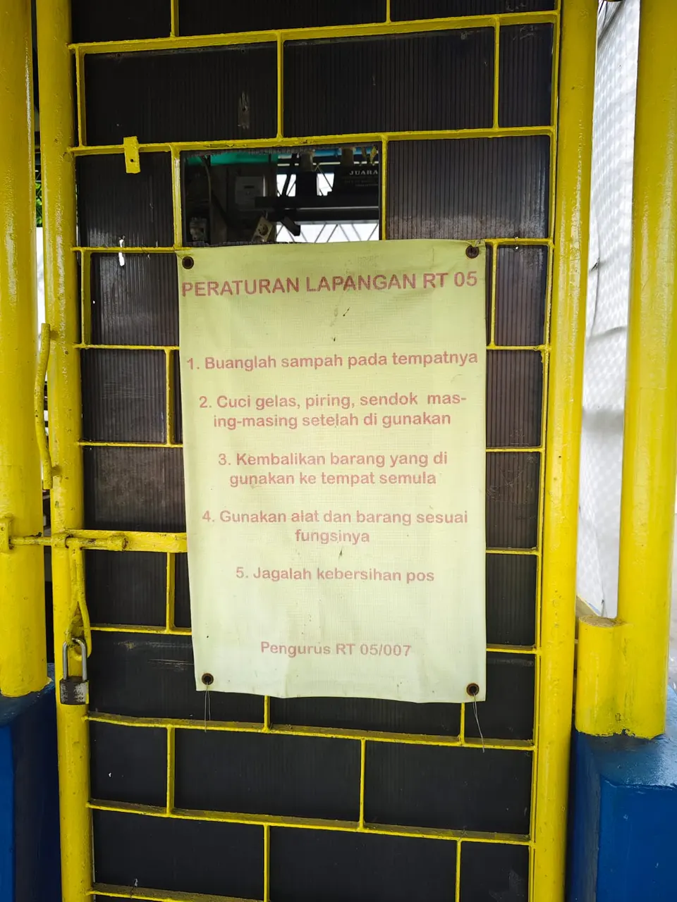 Papan Peraturan Lapangan RT 05 berisi lima aturan, ditandatangani Pengurus RT 05/007.